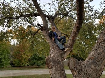 Low section of man sitting on tree trunk against sky