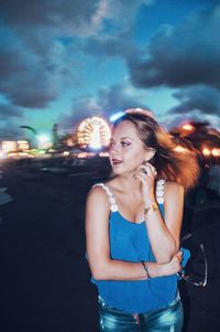 Young woman looking away while standing against cloudy sky at dusk