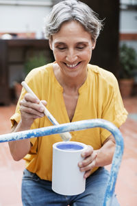 Happy mature woman painting chair at yard