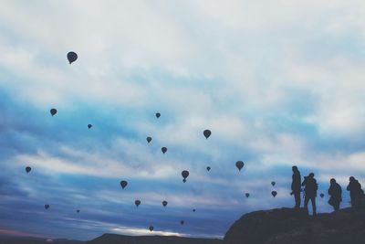 Low angle view of silhouette people with hot air balloons against cloudy sky at cappadocia