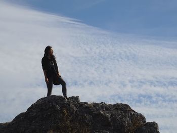 Low angle view of woman standing on rock against cloudy sky