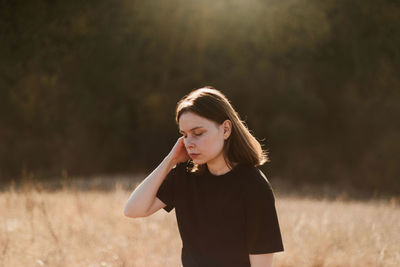 Young woman looking away while standing on field