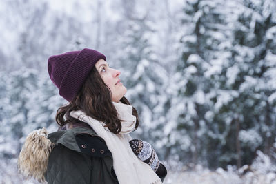 Woman wearing hat standing against trees during winter