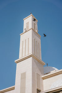 Mosque against blue skies with birds flying around it