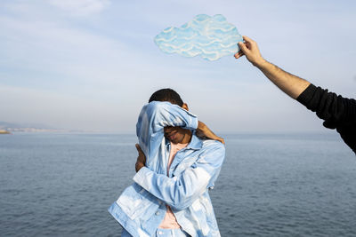 Rear view of friends standing by sea against sky