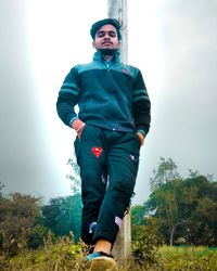 Low angle view of young man looking at camera against sky