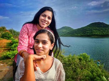 Portrait of smiling young woman against water against sky