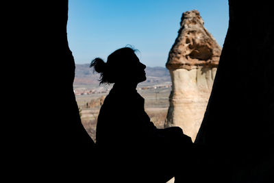 Silhouette woman sitting on rock against sky