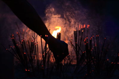 Silhouette of hand amongst incense sticks