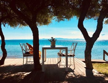 Empty table and chair by sea against sky