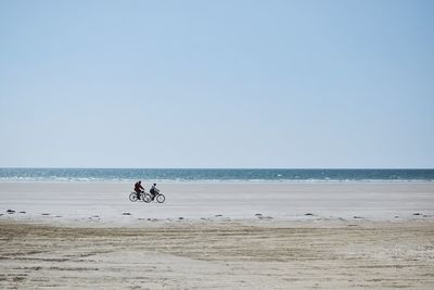 People riding bikes on beach against clear sky