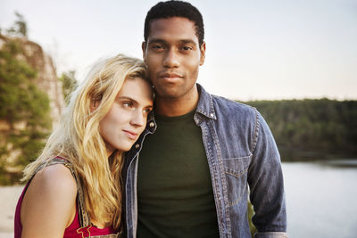 Portrait of confident man standing with woman by lake during sunset