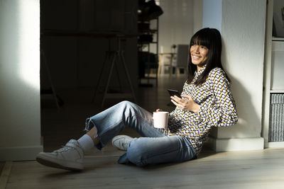 Woman using mobile phone while sitting on floor