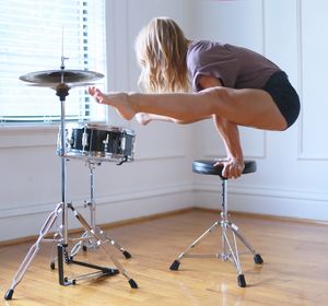 Young woman performing handstand on seat by drum kit at home