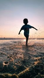 Full length of boy jumping in sea against sky during sunset