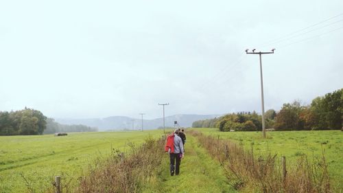 Rear view of people walking on grassy field against sky