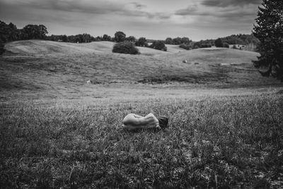 Rear view of depressed naked woman lying on grassy field