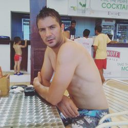 Portrait of shirtless young man looking while sitting on table