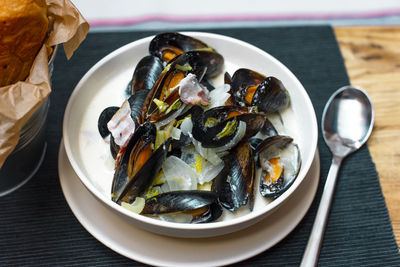 Mussels with onions and bacon in cream sauce in deep plate with bread on the table