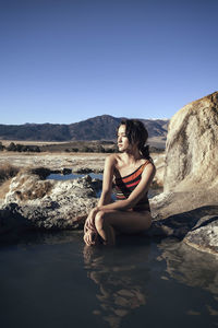 Thoughtful woman sitting on rock at bridgeport hot springs against clear blue sky