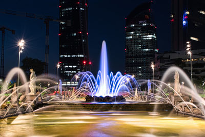 Light trails on fountain against buildings at night