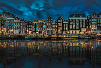 Illuminated buildings reflecting on calm canal in city at dusk