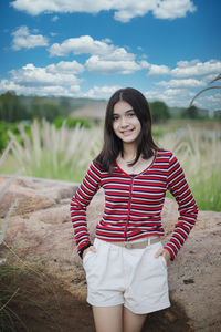 Smiling young woman standing on field against sky