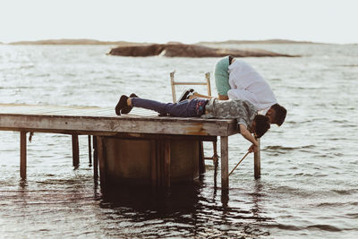 Son fishing while lying on pier by father during summer