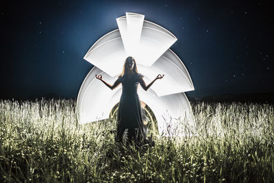 Rear view of woman standing on field against sky at night