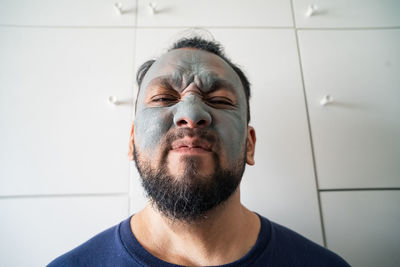 Beauty portrait of a matured asian man over white background, wearing facial cosmetic clay mask.