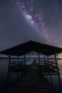 Wooden pier over lake against milky way at night