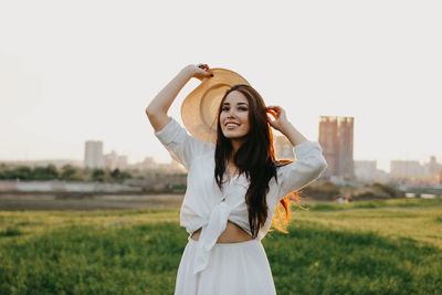 Smiling young woman standing on field against sky