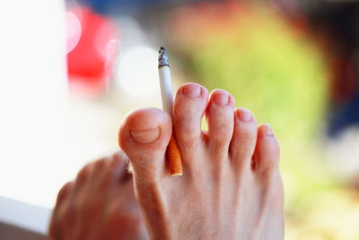 Low section of person holding burning cigarette from leg