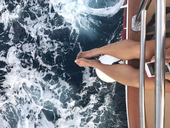 Low section of woman using mobile phone while sitting on boat over sea