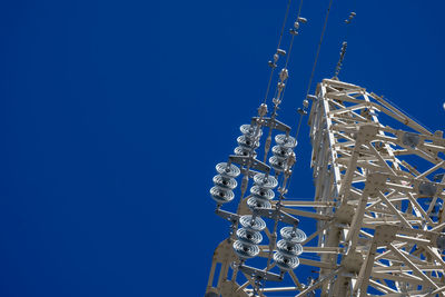 Low angle view of electricity pylon against clear blue sky