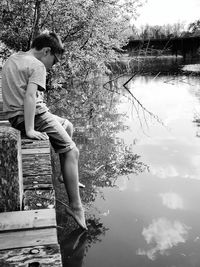 Boy sitting on retaining wall by lake