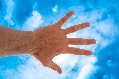 Low angle view of human hand against blue sky