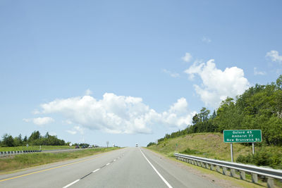 Road sign by highway against sky