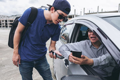 Driver in car showing phone to man on road