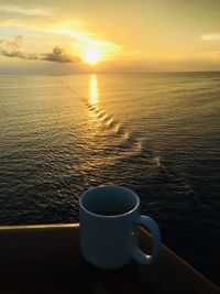 Coffee cup by sea against sky during sunset