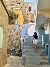 Colourful narrow street of symi island. candid girl climbing up pastel blue stairs. summer. ruins