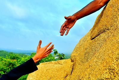 Cropped hand of man reaching towards woman hand against sky