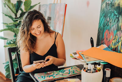 Female painter using smartphone while working on paintings in studio