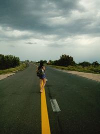 Woman with umbrella on road against sky