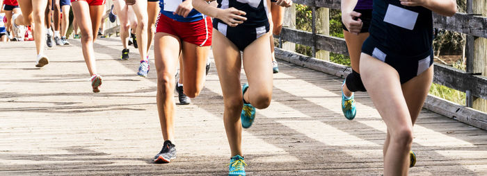 Girls running in a cross country race at sunken meadow state park crossing a wood bridge.