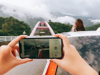 Midsection of woman photographing with mobile phone against sky