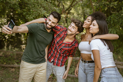 Smiling man taking selfie with friends while standing in forest