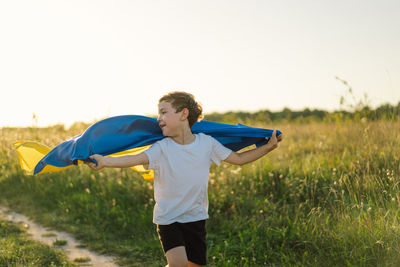 Ukrainian child boy in white t shirt with yellow and blue flag of ukraine in field.