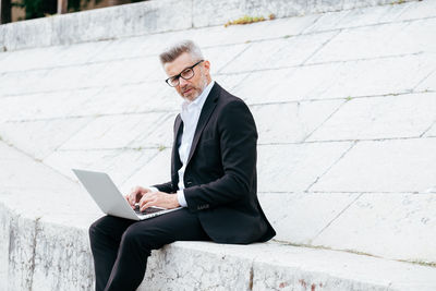 Man using mobile phone while sitting on laptop