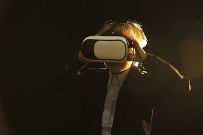 Boy wearing virtual reality simulator against black background